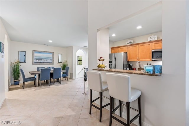 kitchen with stone counters, appliances with stainless steel finishes, a kitchen bar, light tile patterned floors, and kitchen peninsula