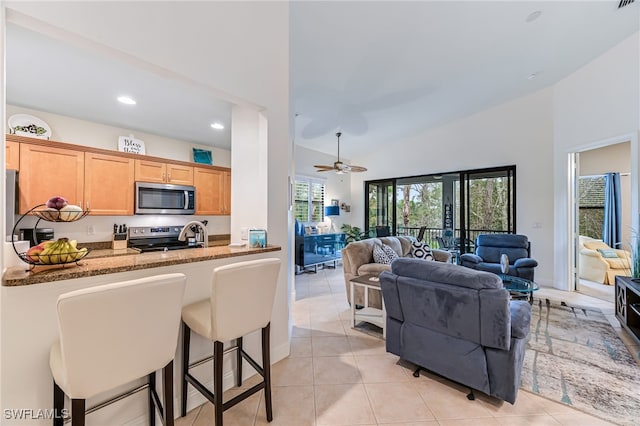 kitchen with ceiling fan, stainless steel appliances, light stone countertops, light tile patterned flooring, and kitchen peninsula