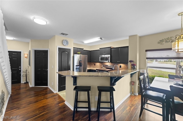 kitchen with appliances with stainless steel finishes, a breakfast bar area, backsplash, kitchen peninsula, and dark wood-type flooring