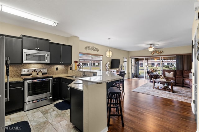 kitchen with sink, a breakfast bar area, hanging light fixtures, kitchen peninsula, and stainless steel appliances