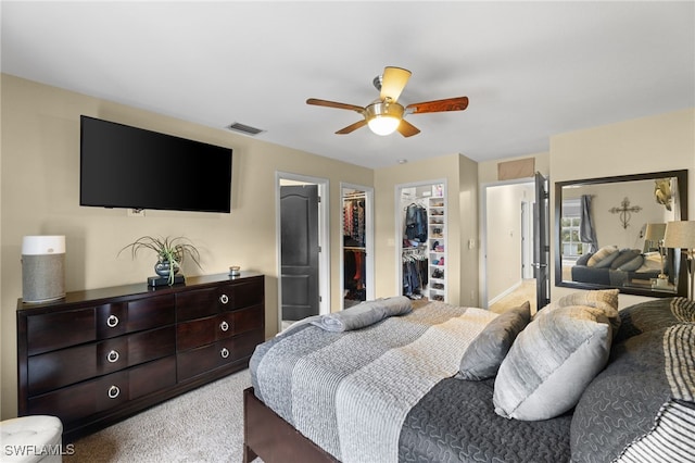 bedroom with a spacious closet, light colored carpet, ceiling fan, and a closet