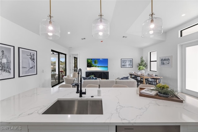 kitchen with decorative light fixtures, sink, light stone counters, and vaulted ceiling