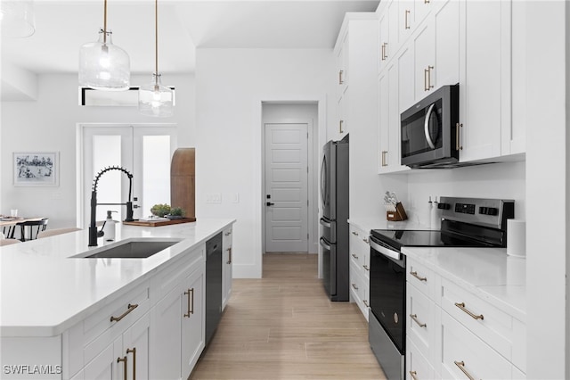 kitchen with white cabinets, appliances with stainless steel finishes, decorative light fixtures, sink, and a center island with sink