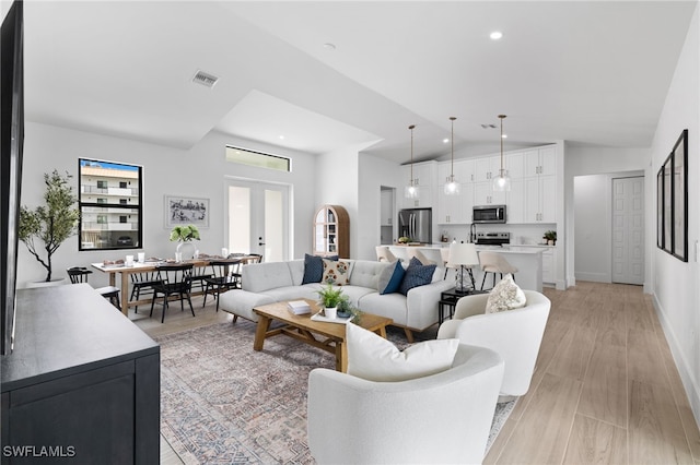 living room featuring light hardwood / wood-style floors, lofted ceiling, and french doors