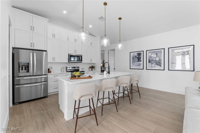 kitchen featuring a kitchen bar, appliances with stainless steel finishes, white cabinets, decorative light fixtures, and an island with sink