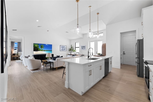 kitchen featuring appliances with stainless steel finishes, decorative light fixtures, sink, white cabinets, and a kitchen island with sink