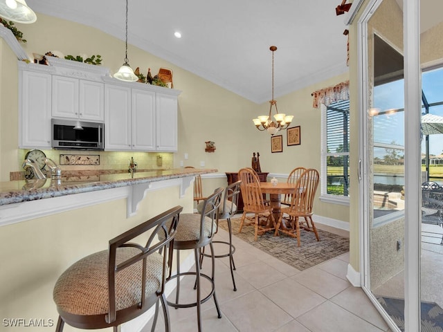 kitchen featuring decorative light fixtures, a breakfast bar area, light stone countertops, and white cabinets