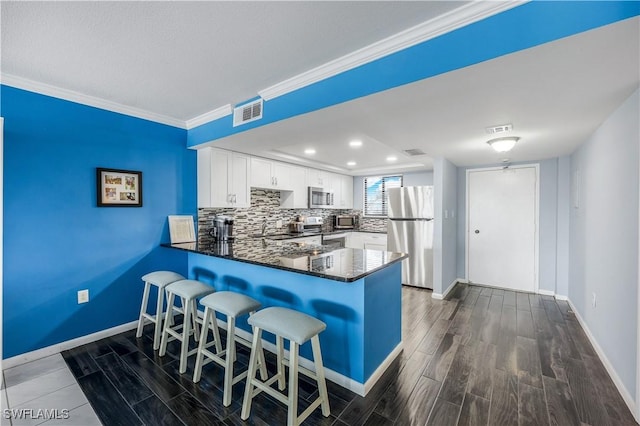 kitchen featuring ornamental molding, kitchen peninsula, white cabinets, stainless steel appliances, and backsplash