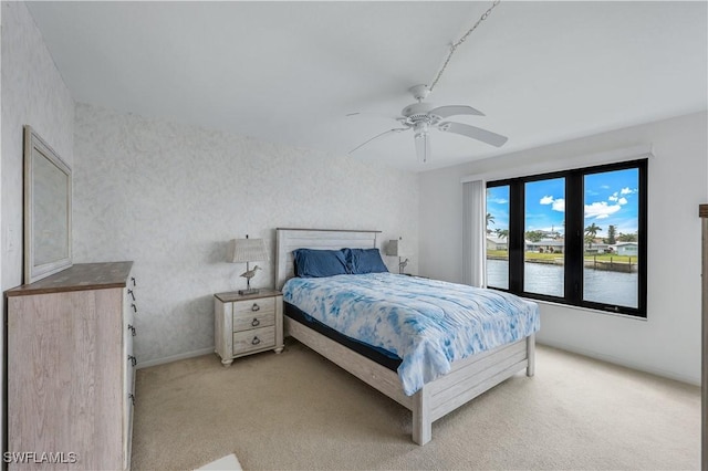 carpeted bedroom featuring ceiling fan and a water view