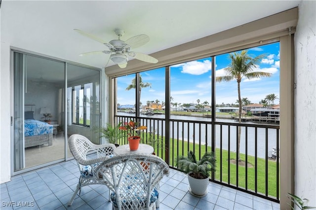 sunroom with ceiling fan and a water view