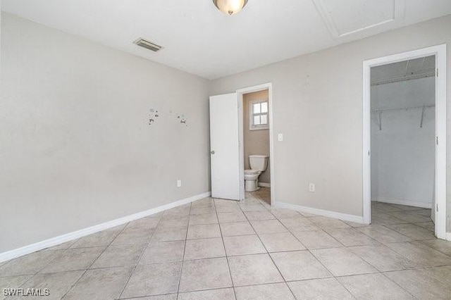 unfurnished bedroom featuring a spacious closet, light tile patterned floors, ensuite bathroom, and a closet