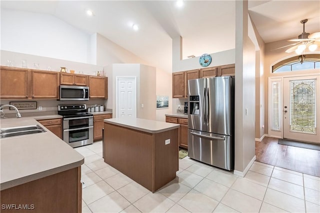 kitchen with sink, high vaulted ceiling, light tile patterned floors, appliances with stainless steel finishes, and a kitchen island