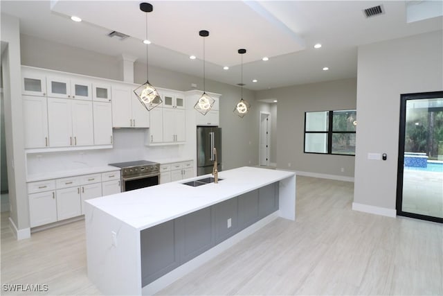 kitchen featuring pendant lighting, sink, a kitchen island with sink, white cabinetry, and premium appliances