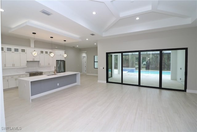 kitchen featuring sink, white cabinets, hanging light fixtures, stainless steel appliances, and a center island with sink