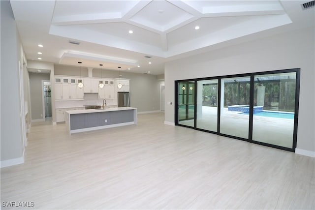 unfurnished living room with a tray ceiling, light hardwood / wood-style floors, and sink