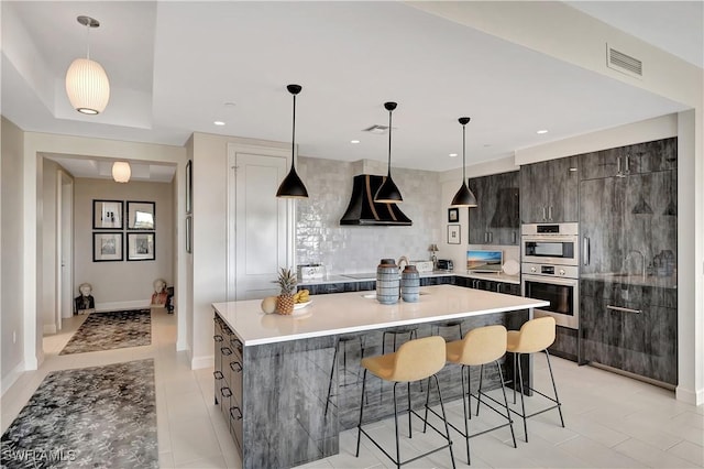 kitchen featuring a breakfast bar area, range hood, dark brown cabinetry, a kitchen island, and decorative light fixtures