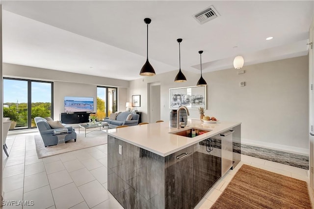 kitchen with pendant lighting, sink, light tile patterned floors, dishwasher, and a kitchen island with sink