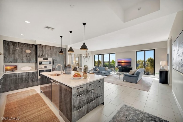 kitchen featuring sink, light tile patterned floors, stainless steel appliances, dark brown cabinets, and a center island with sink