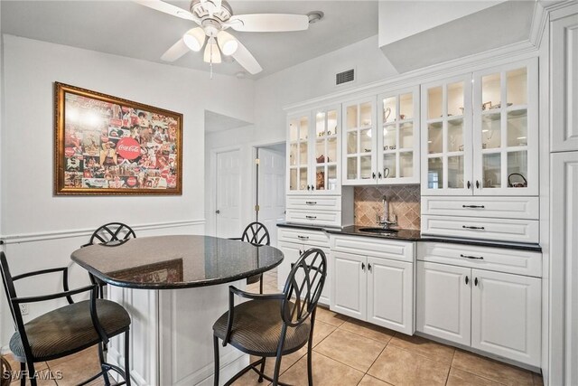 interior space with light tile patterned flooring, sink, tasteful backsplash, ceiling fan, and white cabinets