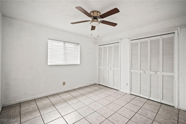 unfurnished bedroom with multiple closets, light tile patterned floors, a textured ceiling, and ceiling fan