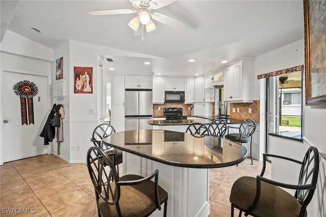 kitchen featuring white cabinets, light tile patterned floors, a breakfast bar area, and black appliances