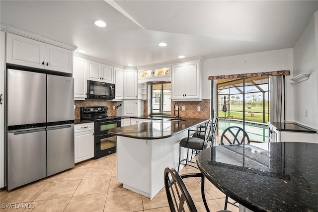 kitchen with light tile patterned flooring, tasteful backsplash, white cabinets, a kitchen breakfast bar, and black appliances