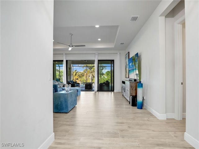 living room with light hardwood / wood-style floors, a raised ceiling, and ceiling fan