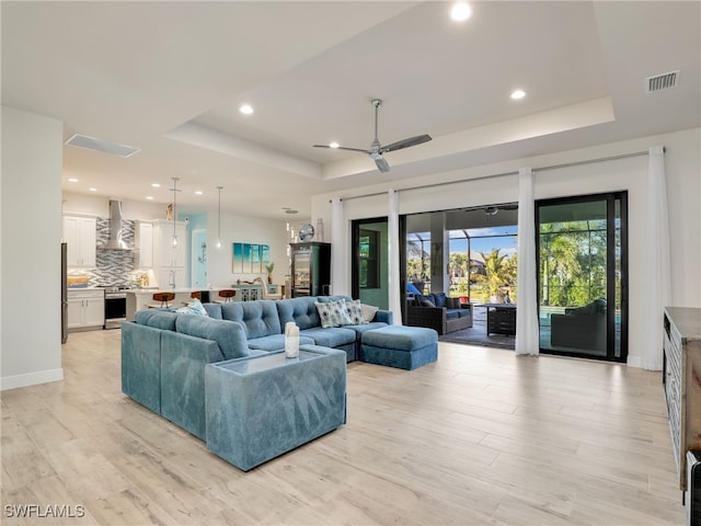 living room with a raised ceiling, ceiling fan, and light wood-type flooring