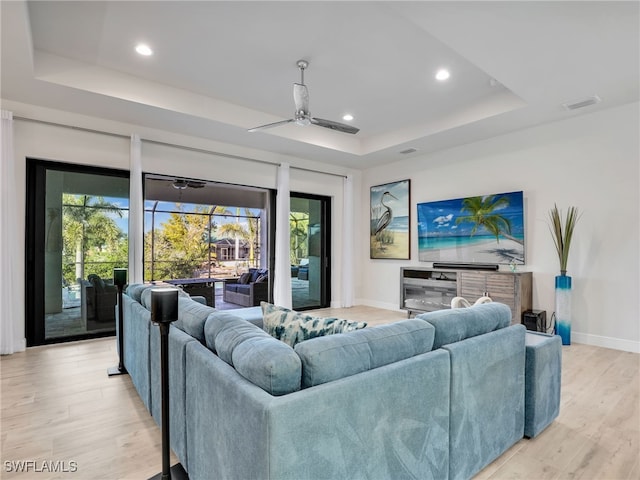 living room featuring light hardwood / wood-style flooring, ceiling fan, and a tray ceiling