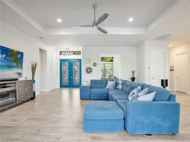 living room featuring a tray ceiling, light hardwood / wood-style floors, french doors, and ceiling fan