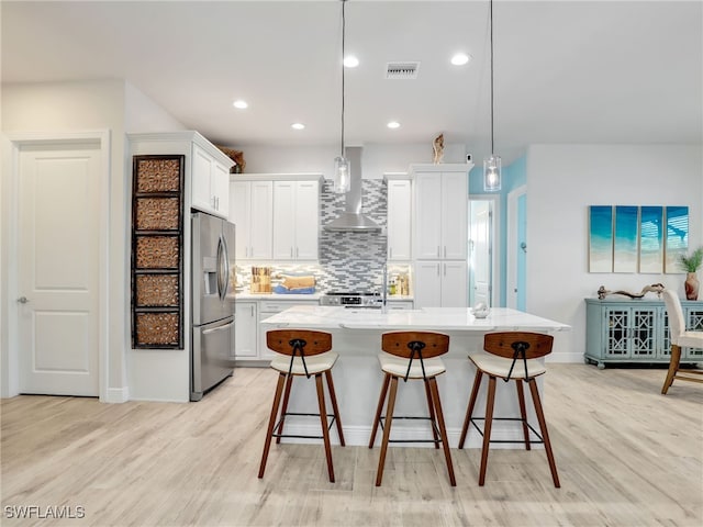 kitchen with appliances with stainless steel finishes, wall chimney exhaust hood, an island with sink, and hanging light fixtures