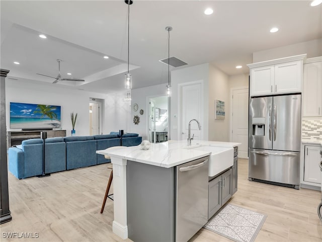 kitchen with tasteful backsplash, an island with sink, sink, white cabinets, and stainless steel appliances