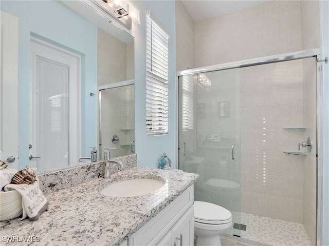 bathroom featuring a shower with door, vanity, and toilet