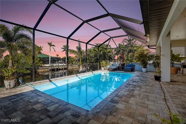 pool at dusk with a patio, a water view, and glass enclosure