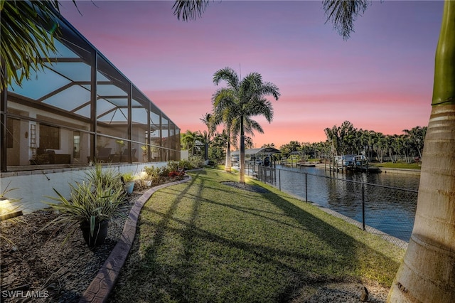 yard at dusk featuring a water view and a lanai