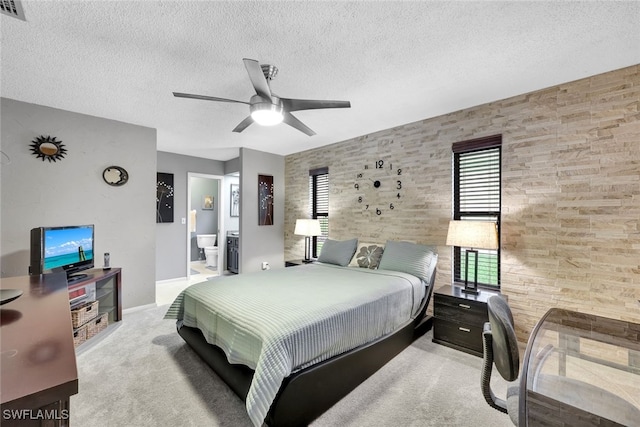 bedroom featuring ceiling fan, connected bathroom, light colored carpet, and a textured ceiling