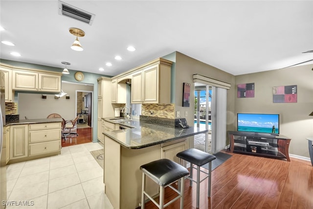 kitchen featuring sink, a kitchen breakfast bar, dark stone counters, hanging light fixtures, and kitchen peninsula