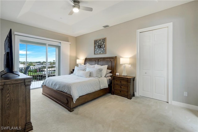 carpeted bedroom with a tray ceiling, access to exterior, ceiling fan, and a closet