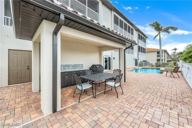 view of patio with grilling area, a fenced in pool, and a balcony