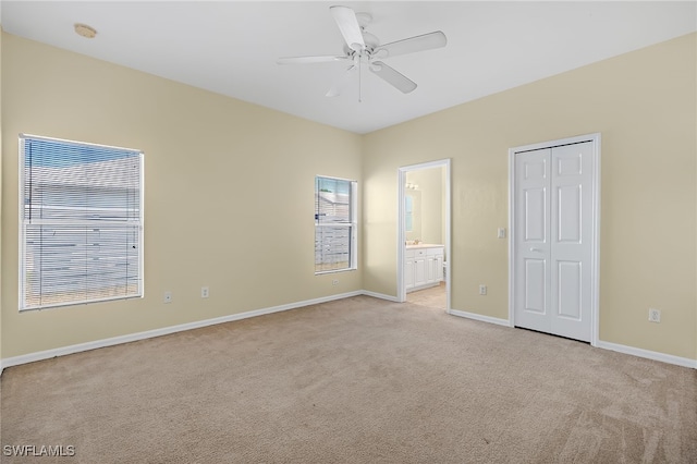 unfurnished bedroom featuring ceiling fan, ensuite bathroom, a closet, and light carpet