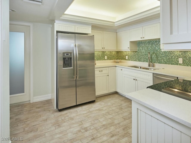 kitchen with tasteful backsplash, light countertops, appliances with stainless steel finishes, light wood-style floors, and a sink