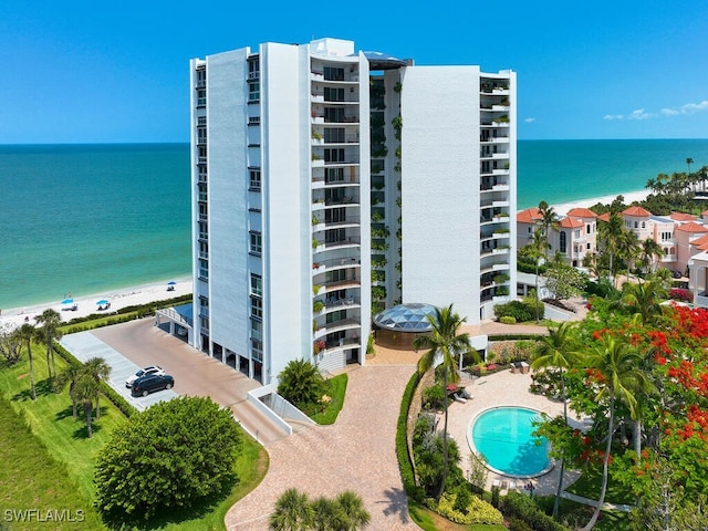 view of building exterior with a community pool, a beach view, and a water view