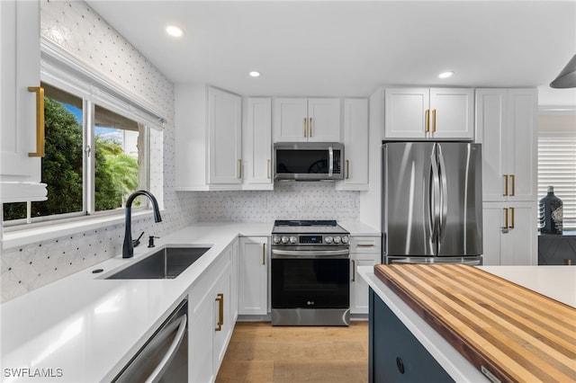 kitchen with butcher block countertops, sink, stainless steel appliances, and white cabinets