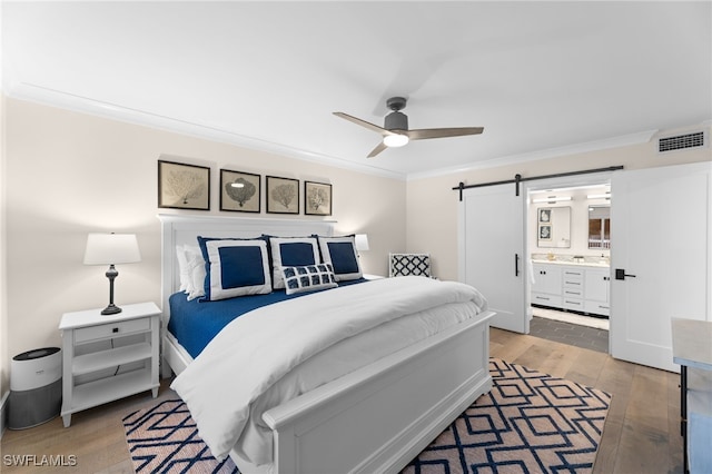 bedroom with ensuite bathroom, wood-type flooring, ornamental molding, ceiling fan, and a barn door