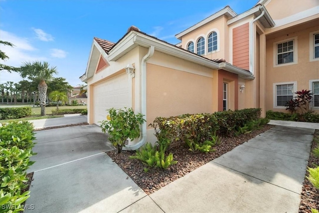 view of side of property featuring a garage, concrete driveway, and stucco siding