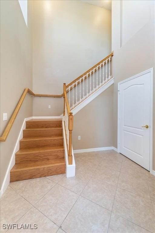 stairs featuring baseboards, a high ceiling, and tile patterned floors