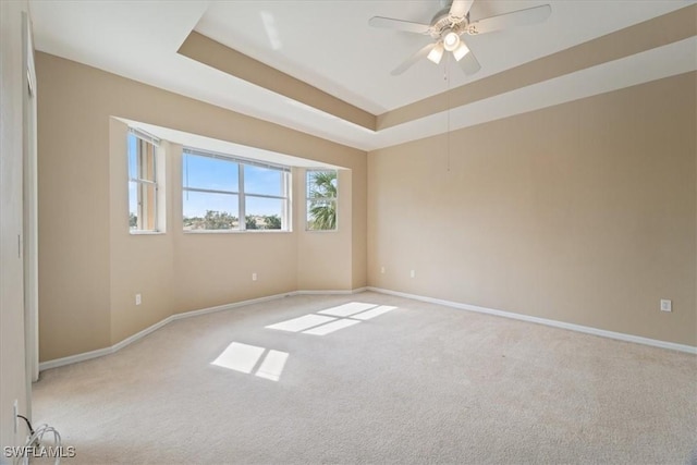 unfurnished room featuring a tray ceiling, light colored carpet, ceiling fan, and baseboards