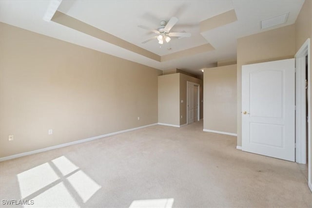 unfurnished bedroom with a raised ceiling, light colored carpet, visible vents, a ceiling fan, and baseboards