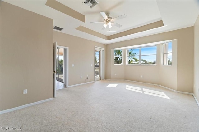 unfurnished room featuring a tray ceiling, plenty of natural light, visible vents, and light colored carpet