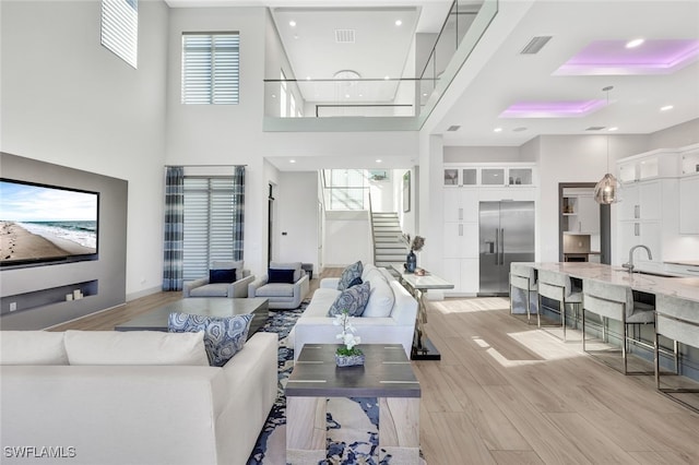 living room with sink, a towering ceiling, a wealth of natural light, and light hardwood / wood-style flooring